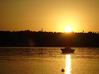 Silhouette of boat on calm sea at golden sunset