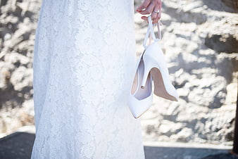 Bride holding white wedding heels in lace dress
