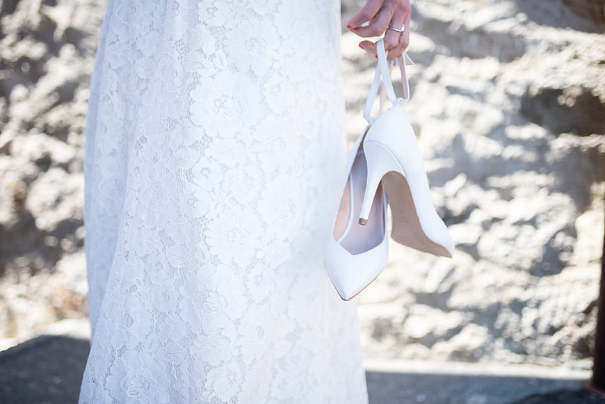 Bride holding white wedding heels in lace dress