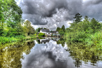 White house by river with dramatic storm clouds and reflection