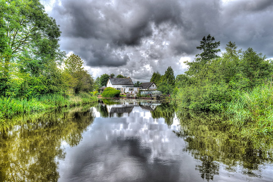 White house by river with dramatic storm clouds and reflection
