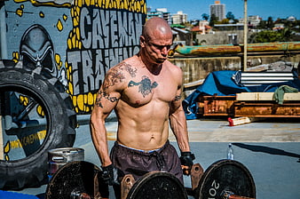 Muscular tattooed man performing farmer's walk with heavy dumbbells