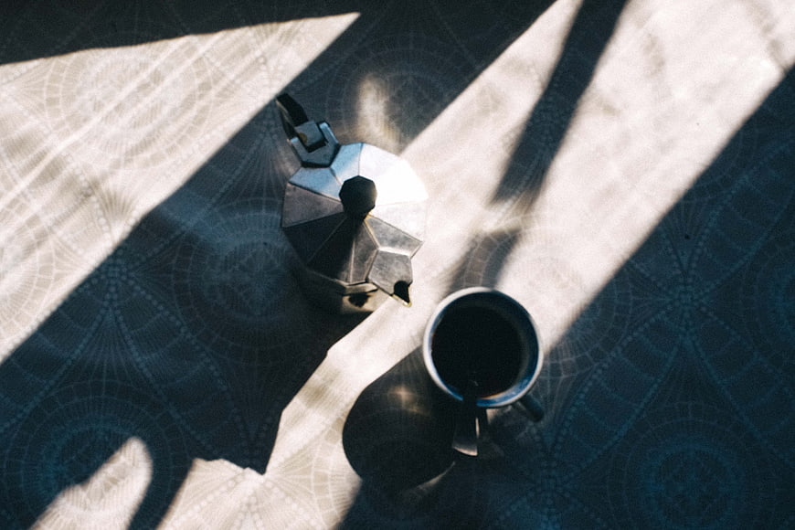 Top view of moka pot and coffee cup on patterned tablecloth