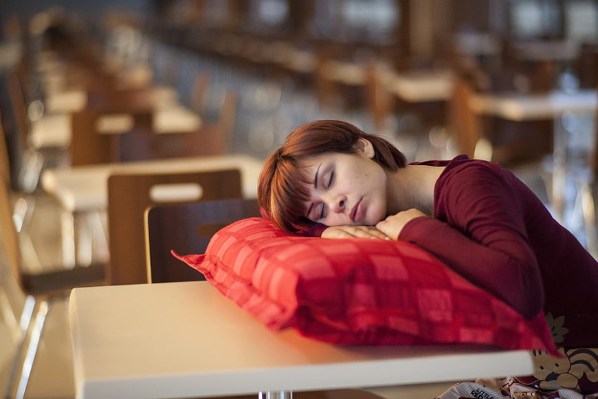 Young woman sleeping on a red pillow at a cafe table