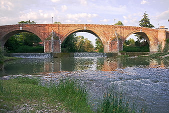 Historic brick arch bridge over a flowing river with weirs