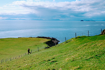 Lone Hiker Walking Green Coastal Hillside Overlooking Ocean