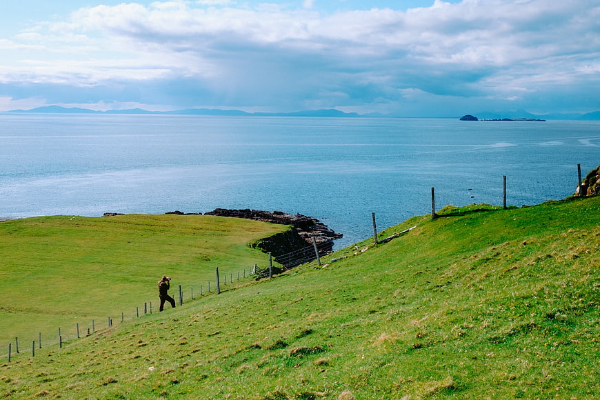 Lone Hiker Walking Green Coastal Hillside Overlooking Ocean