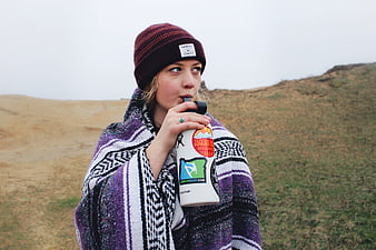 Woman drinking from water bottle wrapped in blanket outdoors