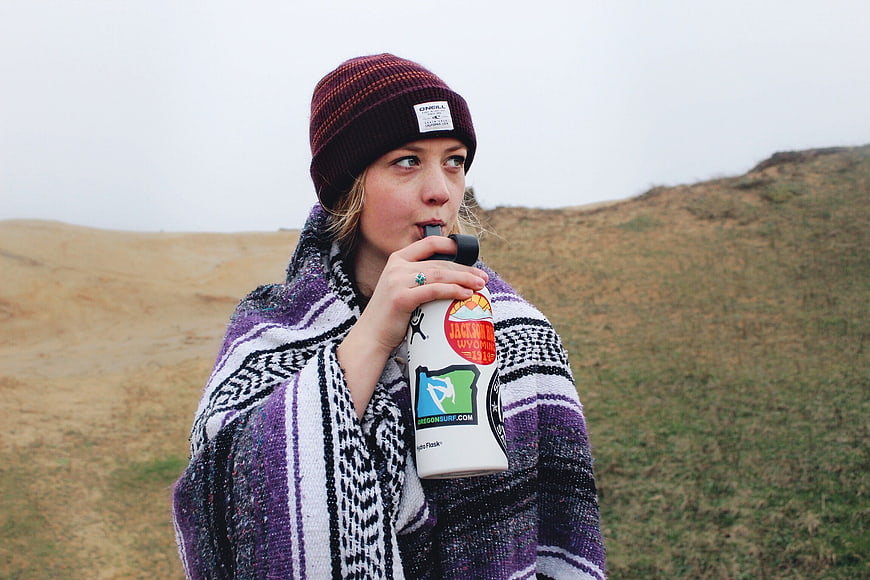 Woman drinking from water bottle wrapped in blanket outdoors