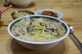 Korean clam noodle soup with side dishes on wooden table