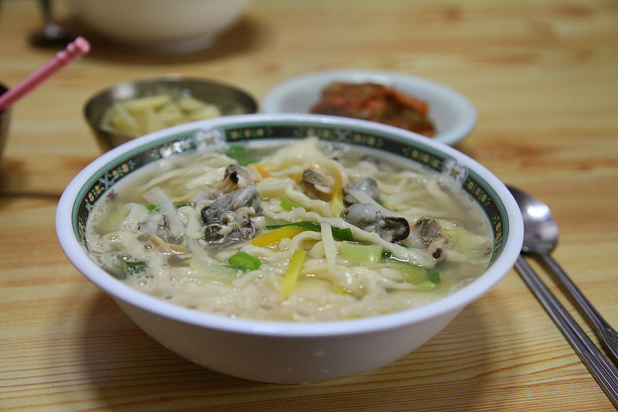Korean clam noodle soup with side dishes on wooden table