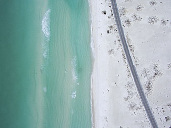 Aerial view of turquoise ocean waves meeting white sandy beach and coastal road