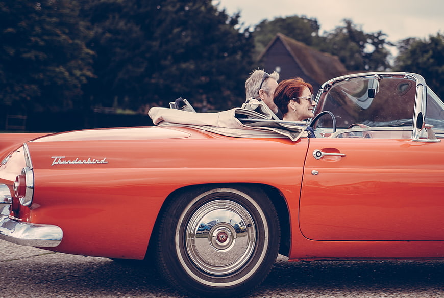 Senior couple driving vintage orange Thunderbird convertible