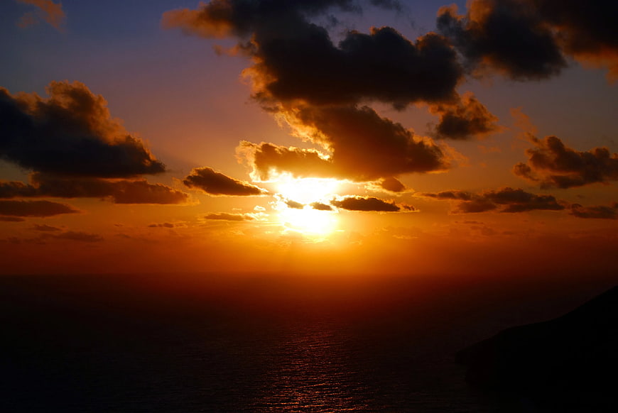 Dramatic Sunset Over Ocean with Golden Sunlight and Clouds