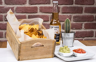 Wooden crate of nachos with Corona beer, salsa, and guacamole on a white table