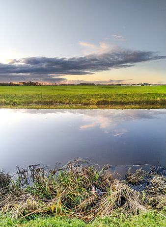 Serene river landscape with green fields and dramatic sunset clouds