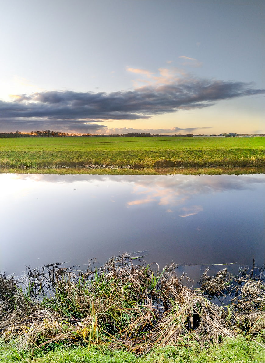 Serene river landscape with green fields and dramatic sunset clouds