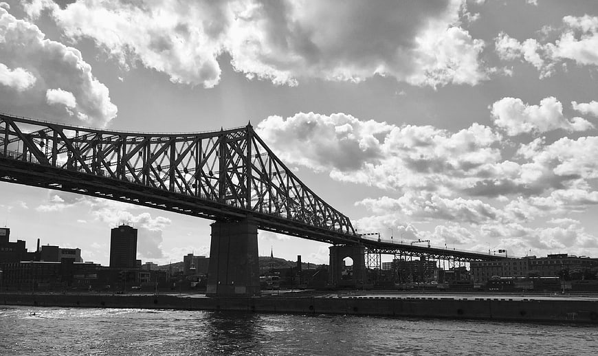 Black and white photo of a large steel truss bridge over a river in a city