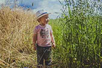 Toddler Boy in Straw Hat Standing in Tall Grass Field