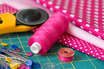 Sewing supplies with pink thread, fabric, and pins on cutting mat