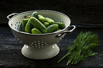 Fresh cucumbers in white colander with dill on dark rustic wooden table
