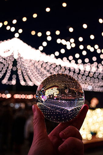Hand holding crystal ball reflecting Christmas lights at night