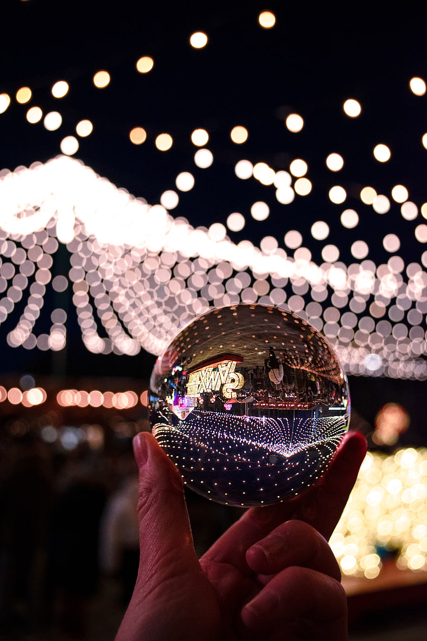 Hand holding crystal ball reflecting Christmas lights at night