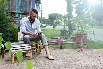 Man with beard sitting on bench using smartphone outdoors