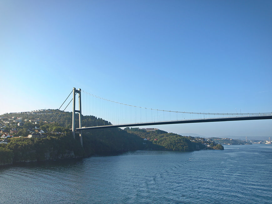 Suspension bridge spanning a fjord with blue sky and green hills