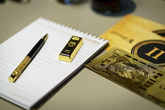 Gold bar, luxury pen, and gold credit card on a notebook