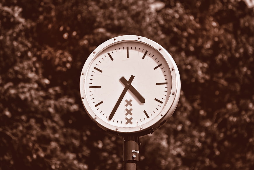 Sepia-toned outdoor clock face against blurred trees