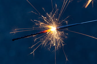 Close-up of burning sparkler with golden sparks against dark blue background