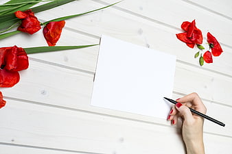 Hand writing on white card with red tulips on wooden table