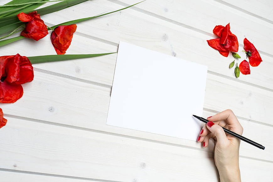 Hand writing on white card with red tulips on wooden table