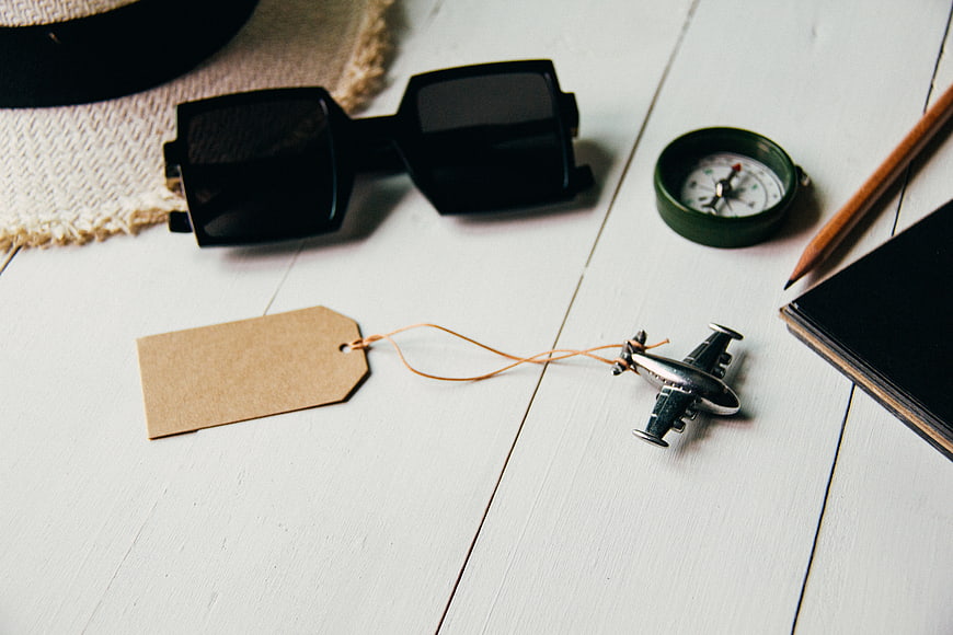 Travel accessories flat lay with sunglasses, compass, and toy airplane