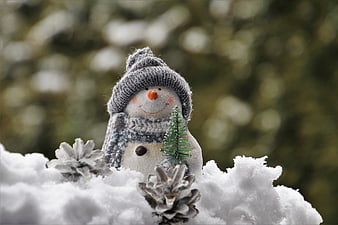 Cute Knitted Snowman Figurine in Snow with Pinecones and Bokeh Background