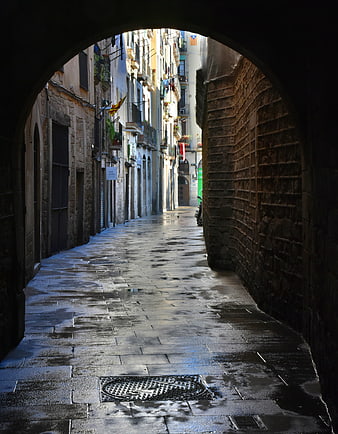 Wet Historic Alleyway Viewed Through Stone Archway in Barcelona