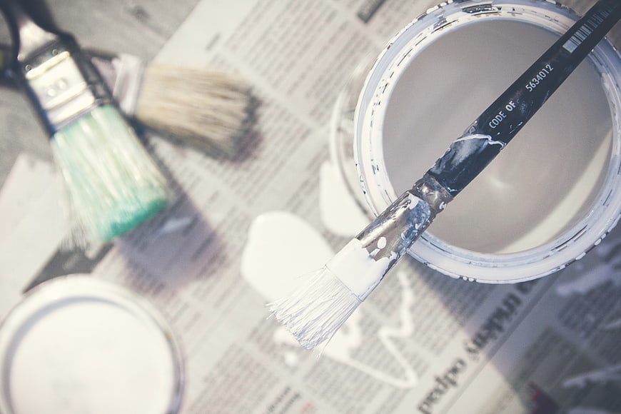 White paint can and brushes on newspaper background