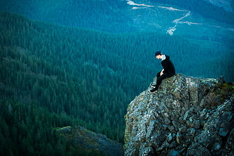 Man sitting on rocky cliff edge overlooking vast blue forest