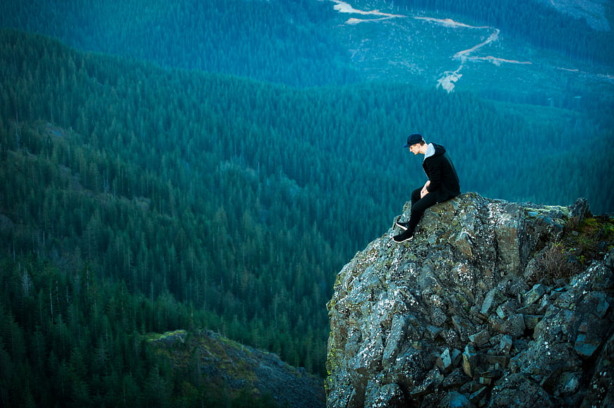 Man sitting on rocky cliff edge overlooking vast blue forest