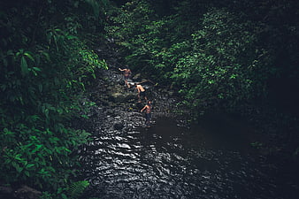 Three men hiking through a dark jungle river stream