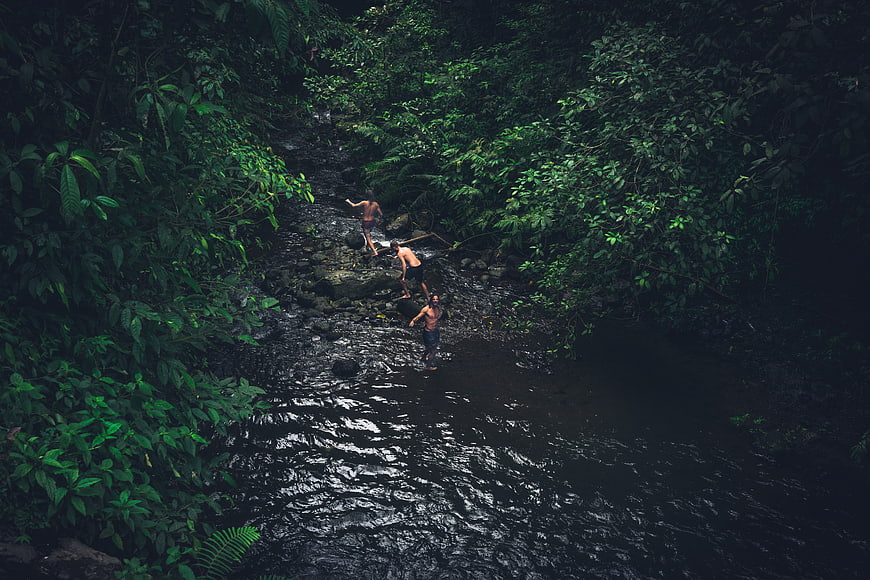 Three men hiking through a dark jungle river stream