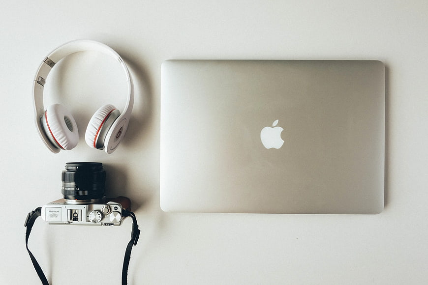 Flat lay of silver laptop, white headphones, and vintage camera