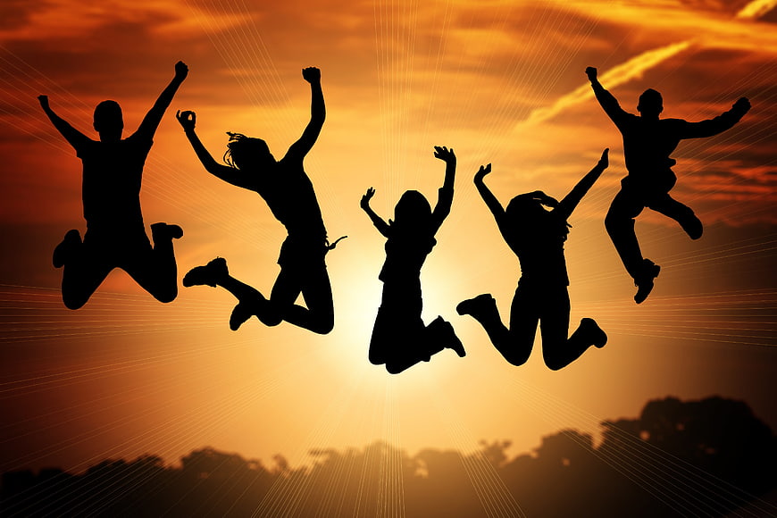 Silhouettes of five people jumping in the air against a vibrant orange sunset sky