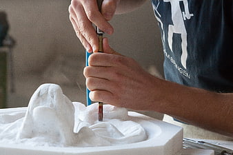 Close-up of hands using a pneumatic chisel to carve a white stone sculpture