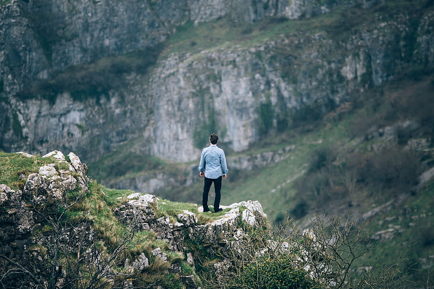 Man standing on rocky cliff edge overlooking mountain valley