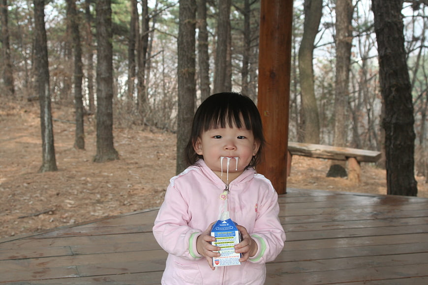 Toddler girl drinking milk with messy mustache in forest