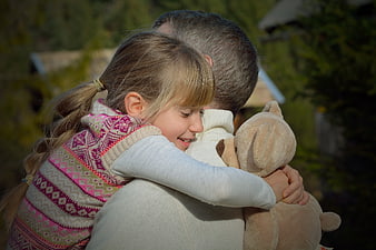 Father and daughter hugging outdoors with teddy bear