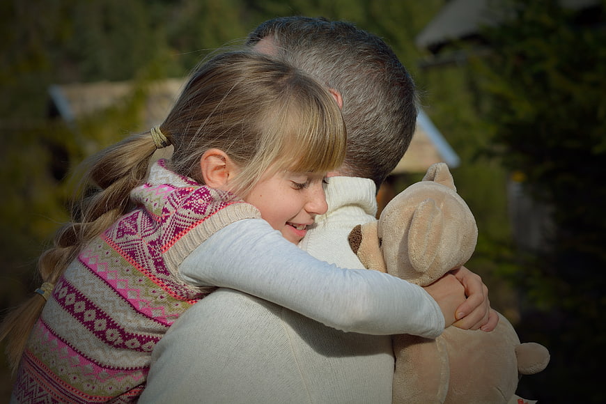 Father and daughter hugging outdoors with teddy bear