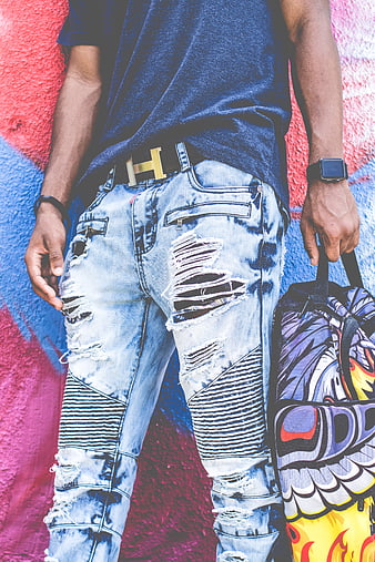 Man in ripped jeans and gold belt against graffiti wall